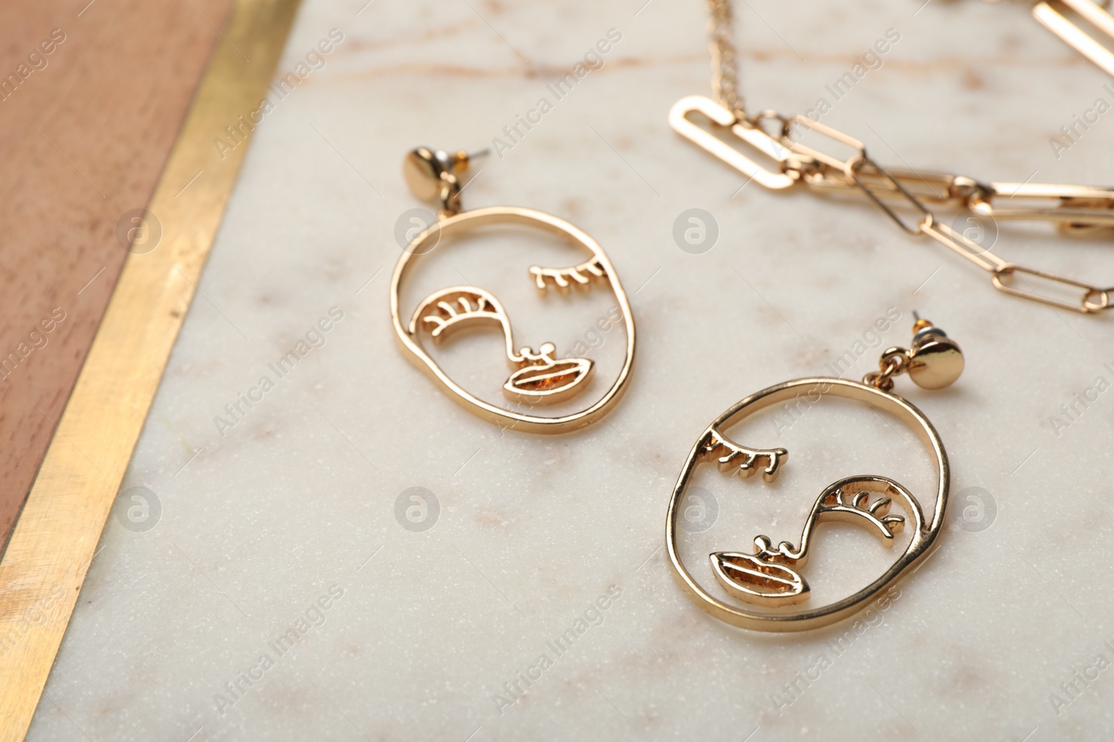 Photo of Face shaped golden earrings on white marble table, closeup. Stylish bijouterie