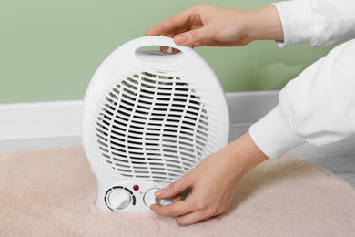 Photo of Woman turning on electric fan heater indoors, closeup