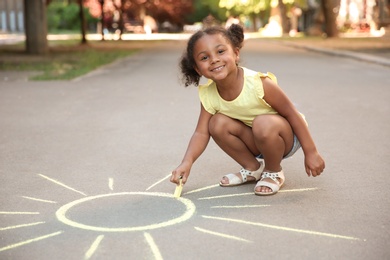 Photo of Little African-American child drawing sun with chalk on asphalt