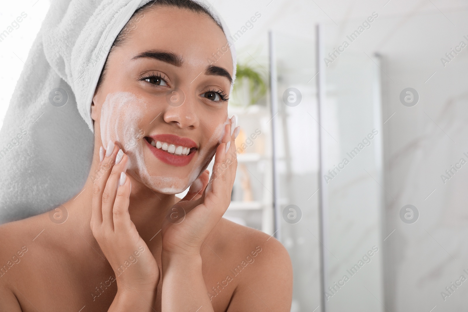 Photo of Beautiful young woman applying cleansing foam onto face in bathroom, space for text. Skin care cosmetic