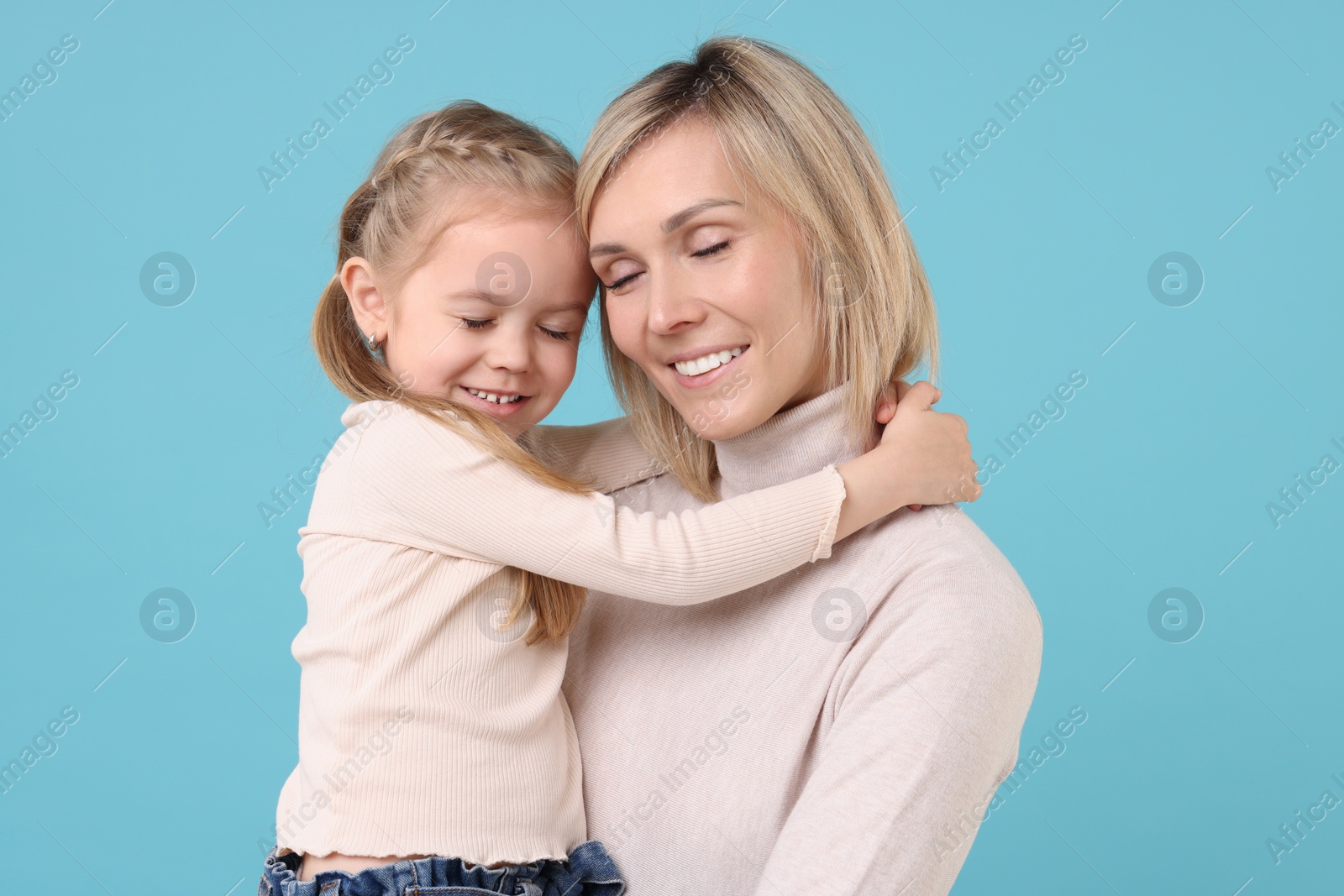 Photo of Daughter hugging her happy mother on light blue background