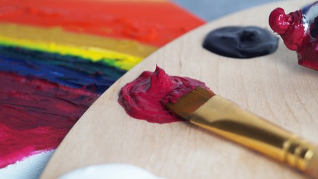 Photo of Artist's palette with colorful samples, brush and canvas with mixed bright paints, closeup