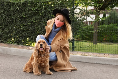 Woman in protective mask with English Cocker Spaniel outdoors. Walking dog during COVID-19 pandemic