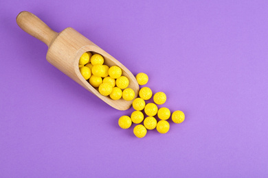 Photo of Delicious lemon chewing gums and scoop on purple background, flat lay