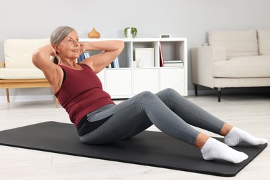 Photo of Senior woman in sportswear doing exercises on fitness mat at home