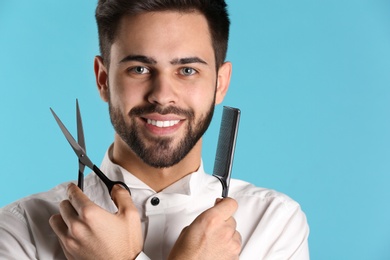 Photo of Young hairstylist holding professional scissors and comb on color background, closeup with space for text