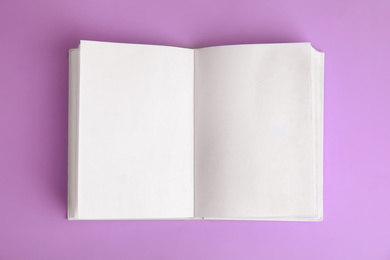 Photo of Open book with blank pages on violet background, top view