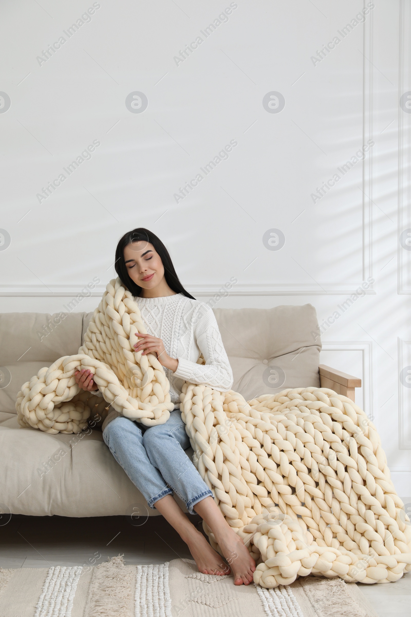 Photo of Young woman with chunky knit blanket on sofa at home