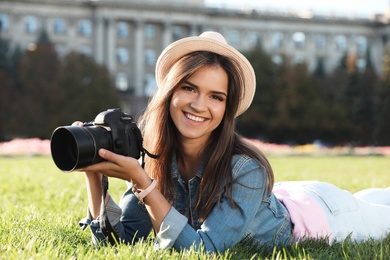 Young female photographer holding professional camera on grass outdoors