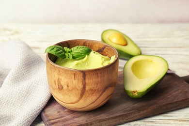 Photo of Bowl with guacamole and ripe avocado on table
