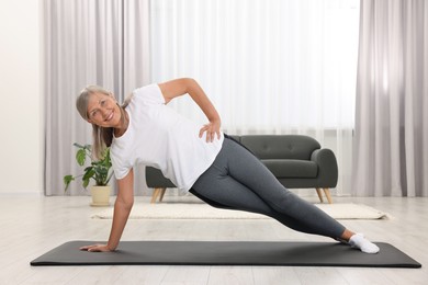 Happy senior woman practicing yoga on mat at home