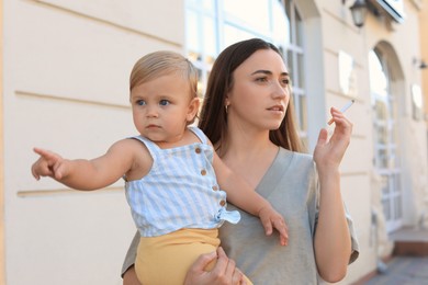 Photo of Mother with cigarette and child outdoors. Don't smoke near kids