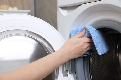 Photo of Woman cleaning empty washing machine with rag indoors, closeup