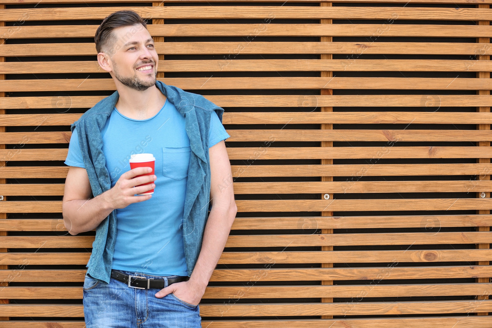 Photo of Portrait of young man with cup of coffee near wooden wall