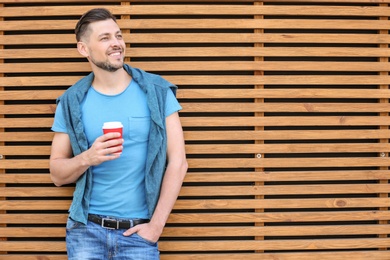 Photo of Portrait of young man with cup of coffee near wooden wall