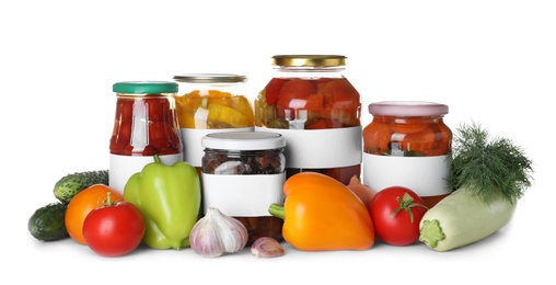 Jars of pickled products and fresh vegetables on white background