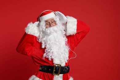 Photo of Merry Christmas. Santa Claus in headphones listening to music on red background, space for text
