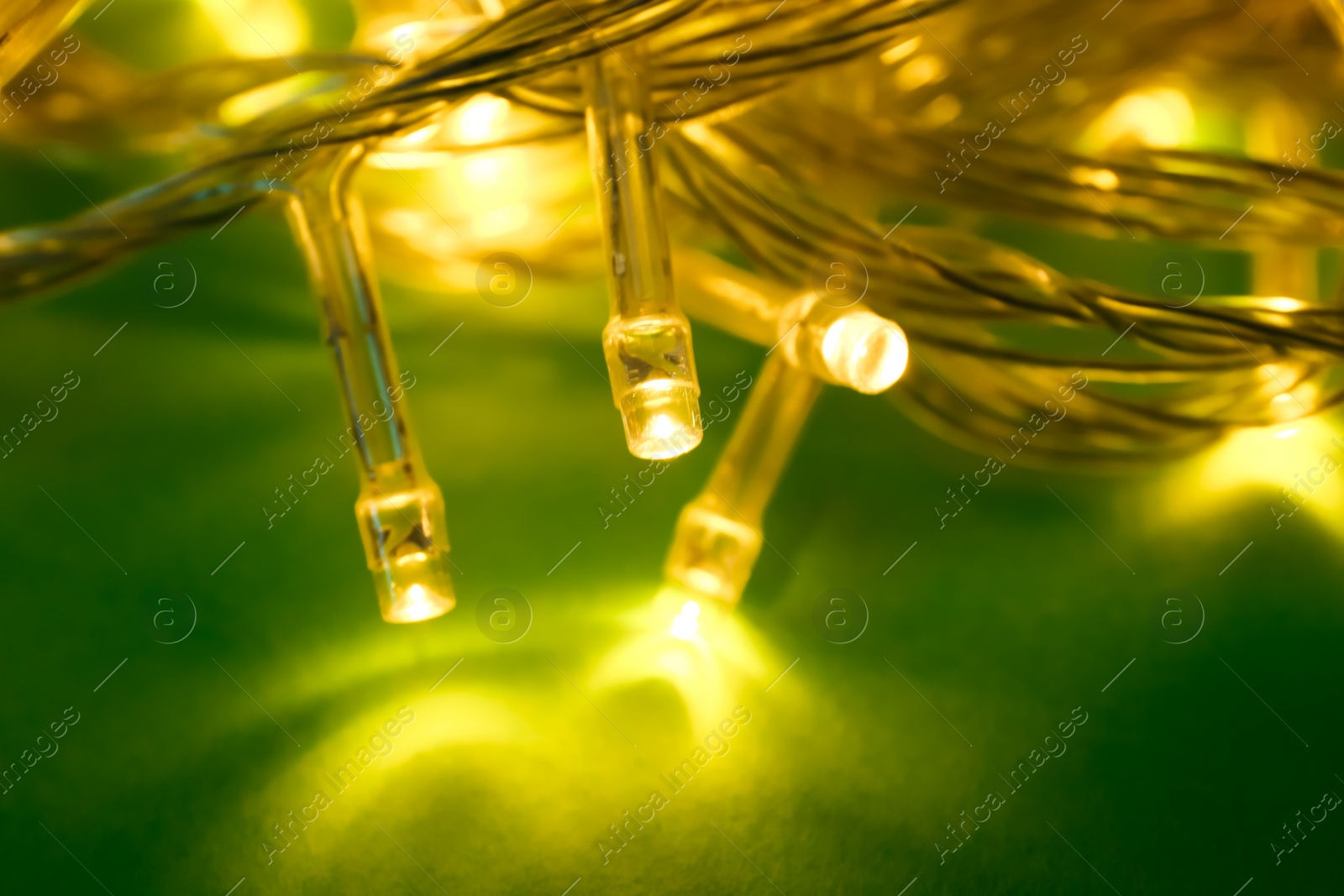 Photo of Glowing Christmas lights on green background, closeup