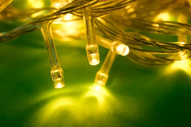 Glowing Christmas lights on green background, closeup