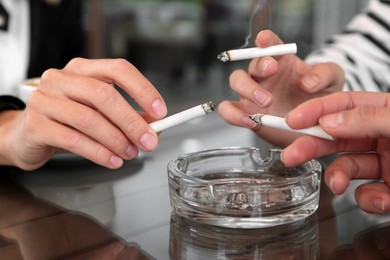 Photo of Women holding cigarette over glass ashtray at table, closeup