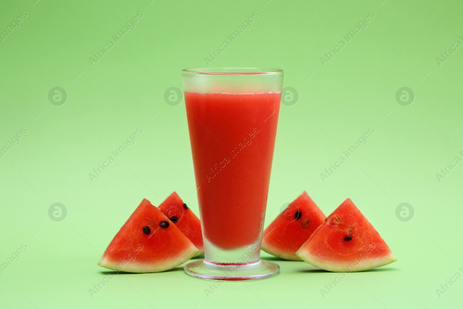Photo of Glass of delicious drink and cut fresh watermelon on light green background