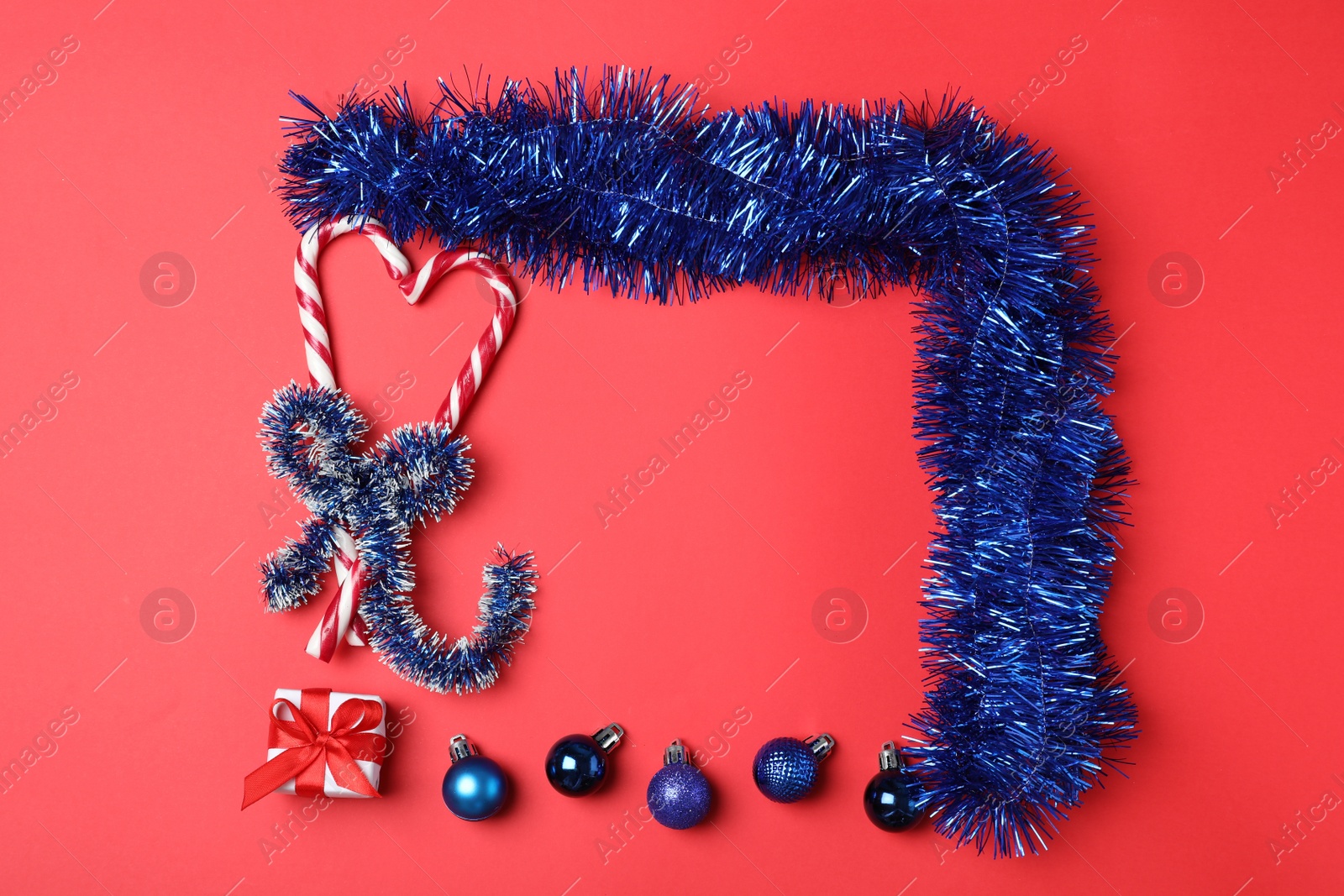 Photo of Frame of bright blue tinsel and Christmas decor on red background, flat lay. Space for text