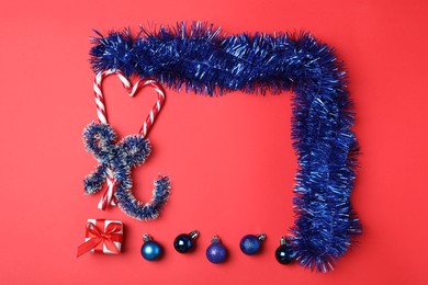 Photo of Frame of bright blue tinsel and Christmas decor on red background, flat lay. Space for text