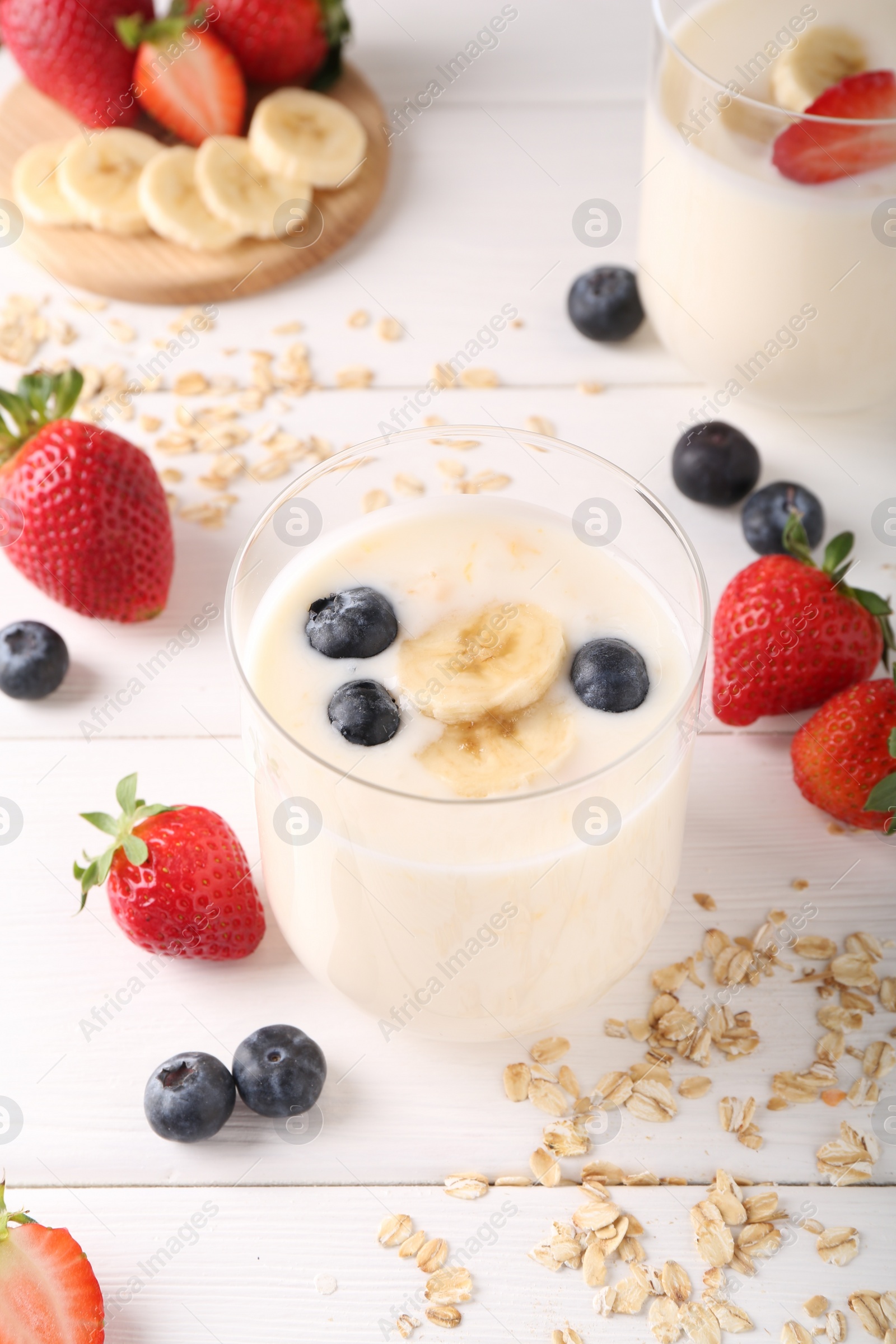 Photo of Healthy break. Composition with tasty yogurt, banana and berries in glasses on white wooden table