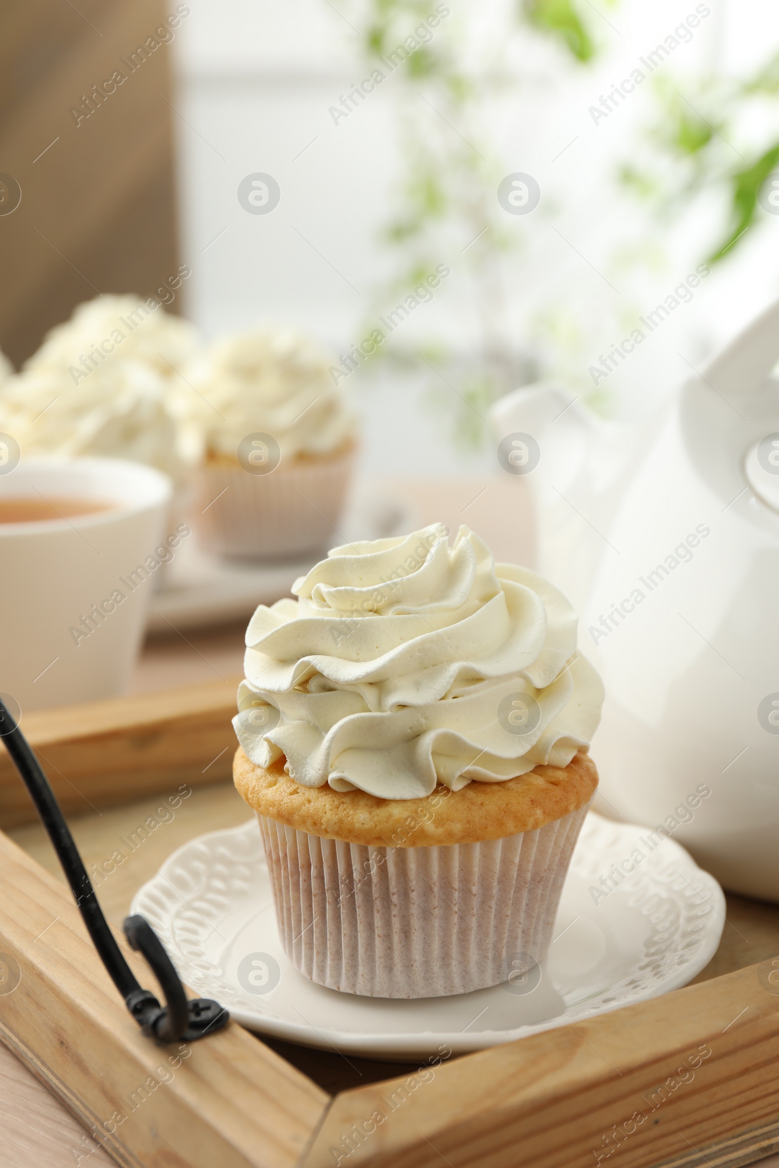 Photo of Tasty cupcake with vanilla cream and teapot on wooden tray, closeup