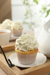 Tasty cupcake with vanilla cream and teapot on wooden tray, closeup