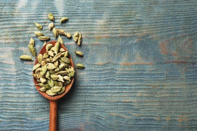 Photo of Spoon with dry cardamom on blue wooden table, top view. Space for text