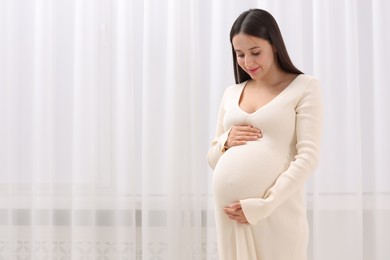 Photo of Beautiful pregnant woman in white dress indoors, space for text