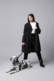 Beautiful young woman with her adorable Dalmatian dog on light grey background. Lovely pet