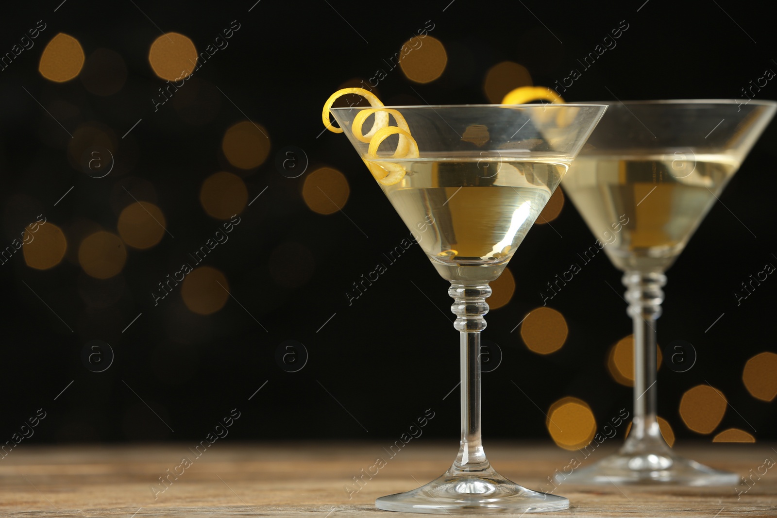 Photo of Glasses of Lemon Drop Martini cocktail with zest on wooden table against blurred background. Space for text