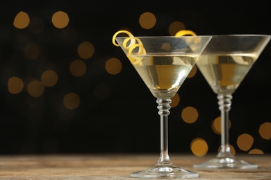 Photo of Glasses of Lemon Drop Martini cocktail with zest on wooden table against blurred background. Space for text