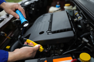 Mechanic with flashlight fixing car outdoors, closeup