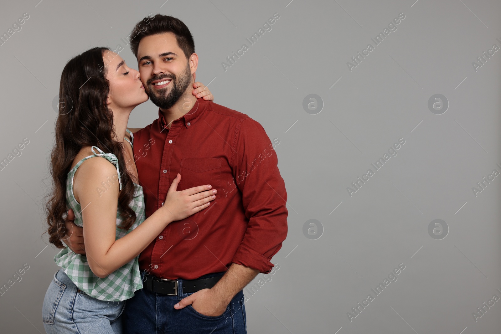 Photo of Woman kissing her smiling boyfriend on grey background. Space for text