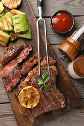 Photo of Delicious grilled beef steak and vegetables served on wooden table, flat lay