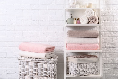 Photo of Shelving unit and baskets with clean towels and toiletries near brick wall