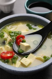 Photo of Bowl of delicious miso soup with tofu and spoon on table, closeup