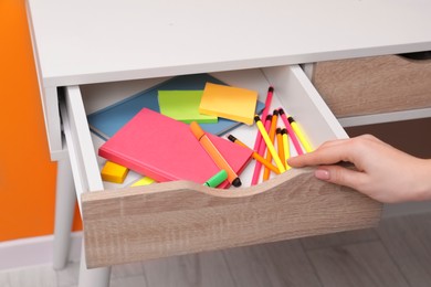 Photo of Woman opening desk drawer with office supplies indoors, closeup