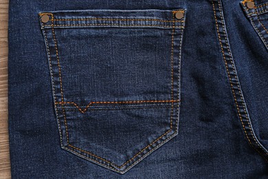 Photo of Stylish dark blue jeans on wooden background, closeup of back pocket