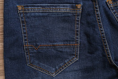 Stylish dark blue jeans on wooden background, closeup of back pocket