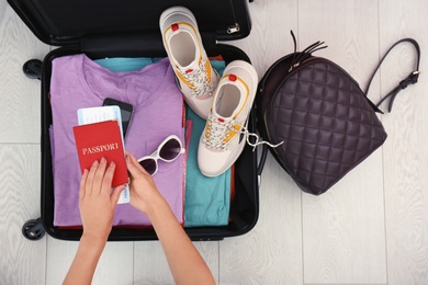 Photo of Woman packing suitcase for journey on wooden floor, top view