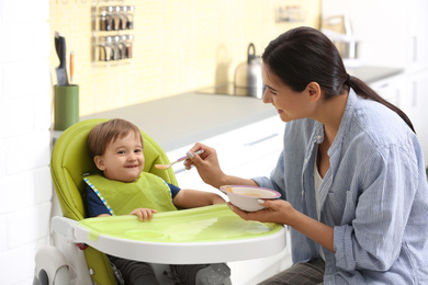 Photo of Young nanny feeding cute little baby in kitchen