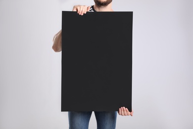 Man holding blank poster on light grey background, closeup