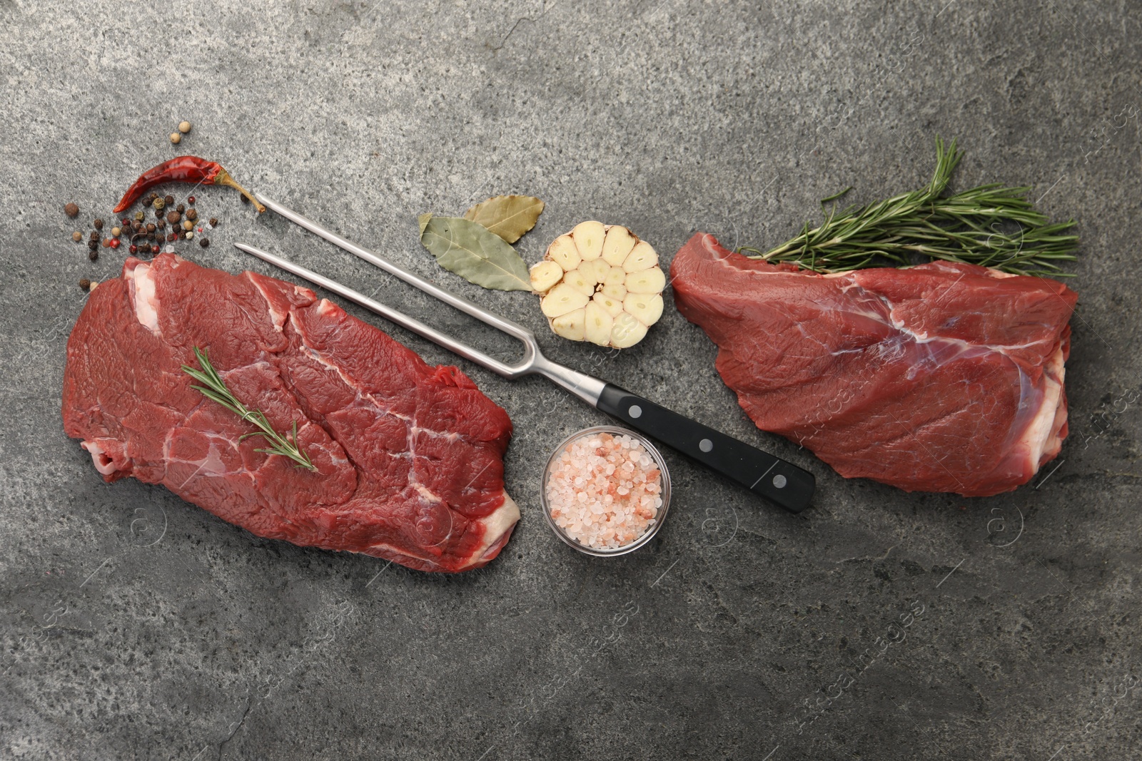 Photo of Piece of raw beef meat, spices, rosemary and fork on grey table, flat lay