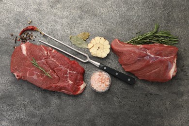 Piece of raw beef meat, spices, rosemary and fork on grey table, flat lay