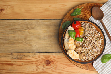 Photo of Tasty buckwheat porridge with meat and mushrooms on wooden table, flat lay. Space for text