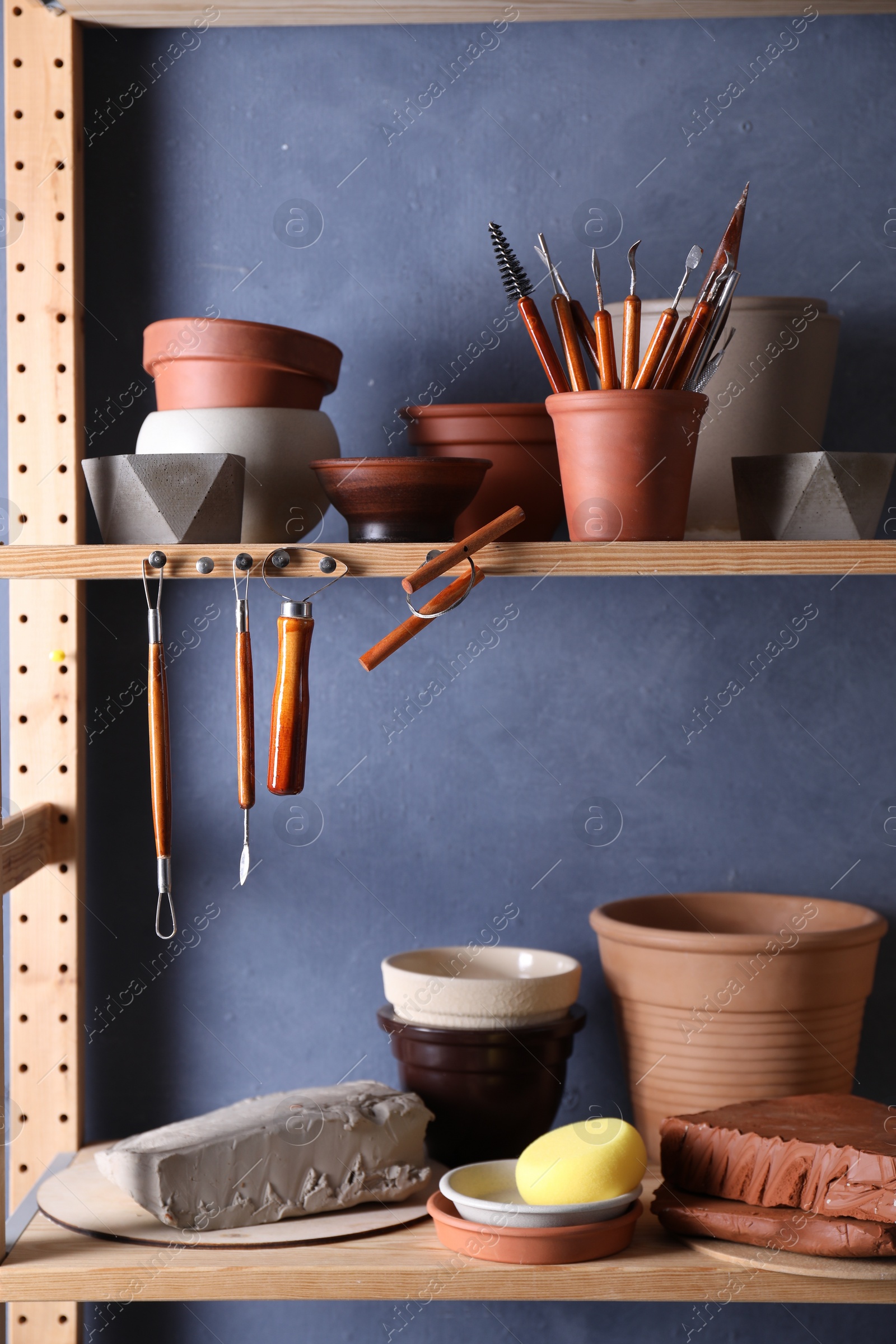 Photo of Set of different crafting tools and clay dishes on wooden rack in workshop